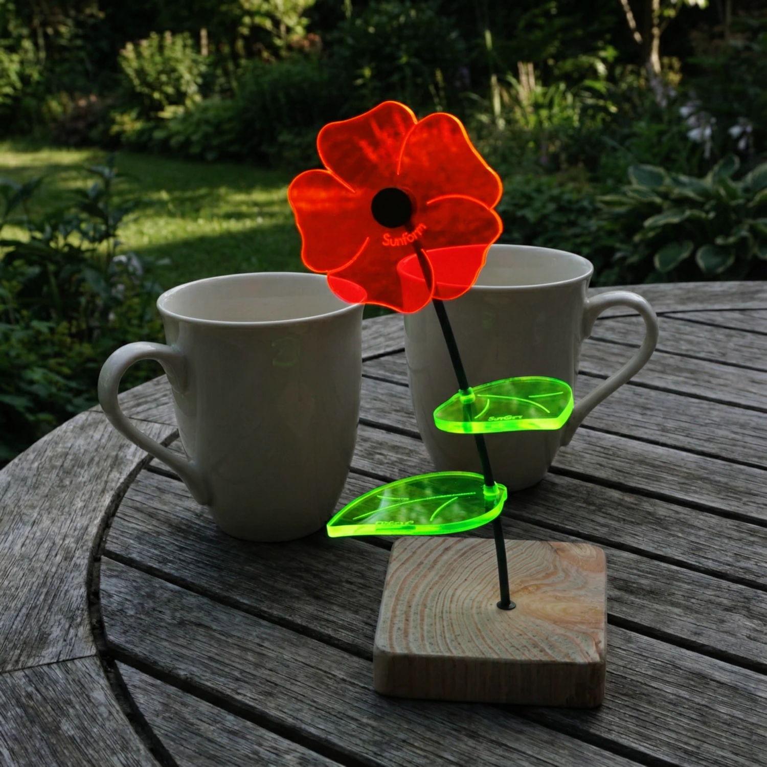 Little Susi 1 SunForm-Sonnenfänger Sonnenfängerin Little Susi mit Standfuß auf einem vergrauten Terrassentisch mit 2 Kaffeebechern im Hintergrund