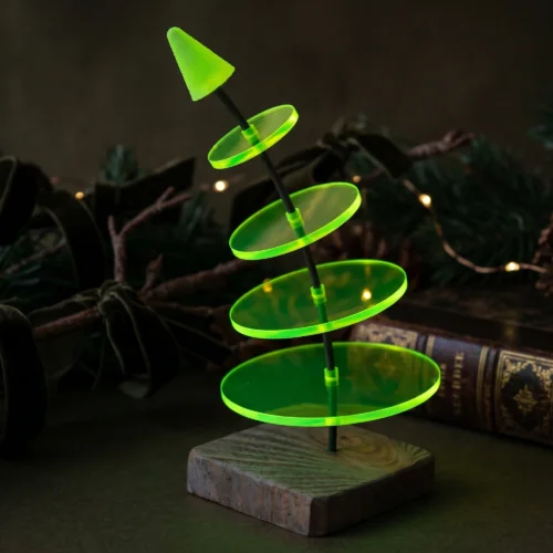 Sonnenfänger - Weihnachtsbaum: "Little Noel" 14 SunForm-Sonnenfänger Sonnenfänger-Weihnachtsbaum als Weihnachtsdeko vor einem Tannenzweig mit Lichterkette und Buch